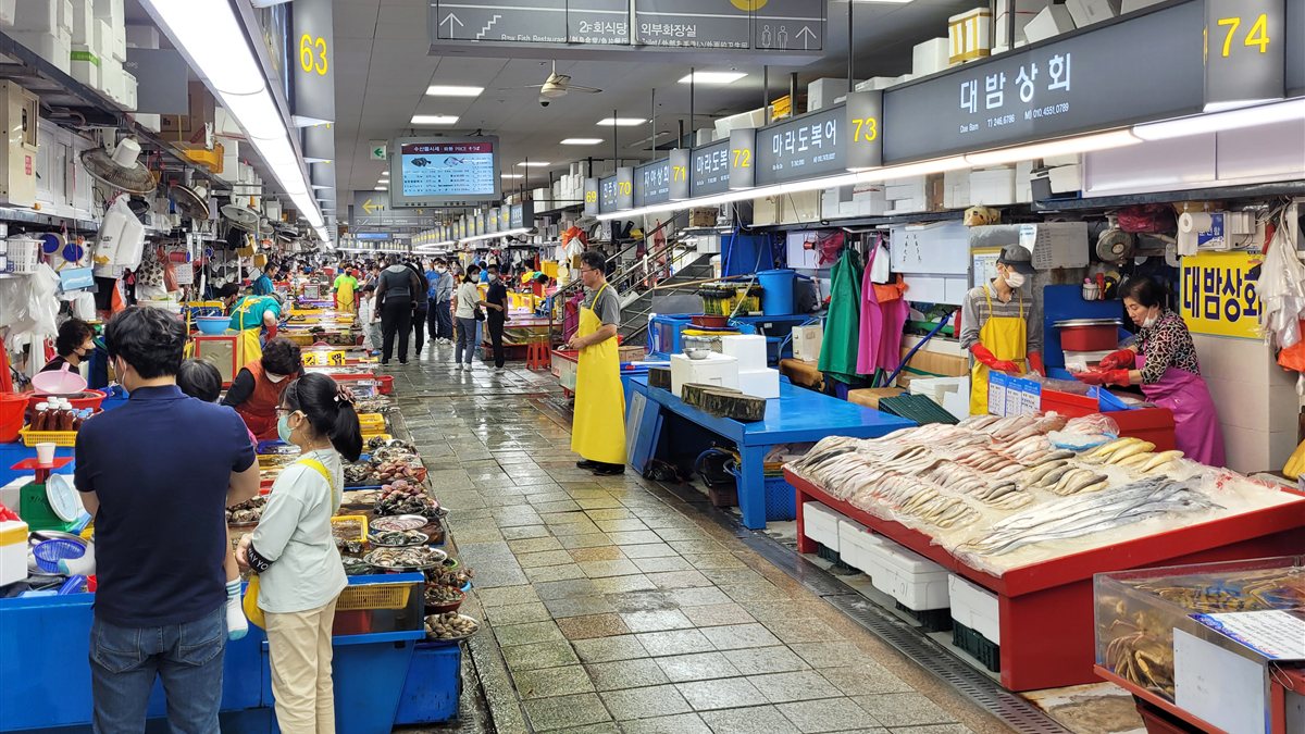 Fish stalls and shoppers along an indoor aisle at Jagalchi Market