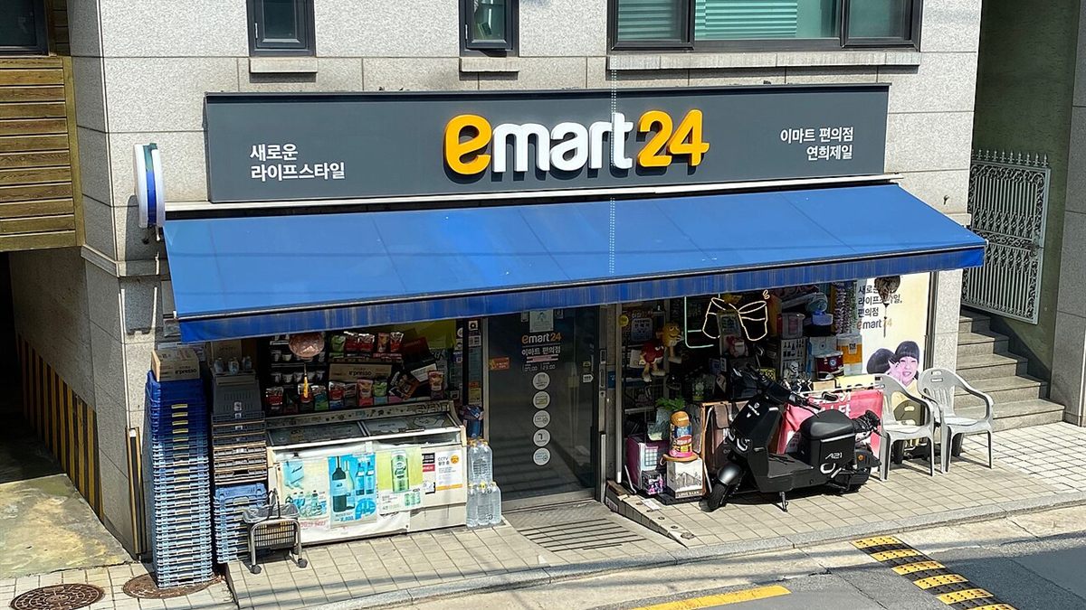 An Emart24 convenience store with a blue awning on a street in Korea