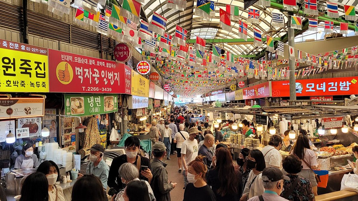 Inside Gwangjang Market in Seoul: food stalls with Korean signs under strings of flags