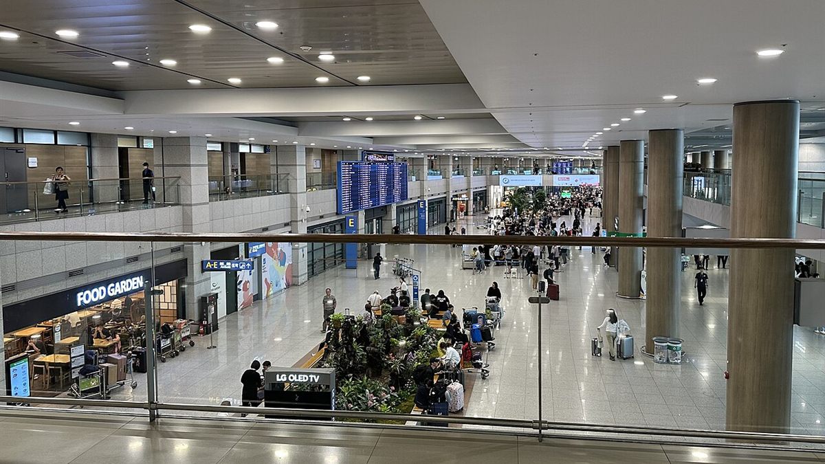 Arrivals hall of Incheon Airport Terminal 1, seen from the floor above, with travelers and luggage trolleys