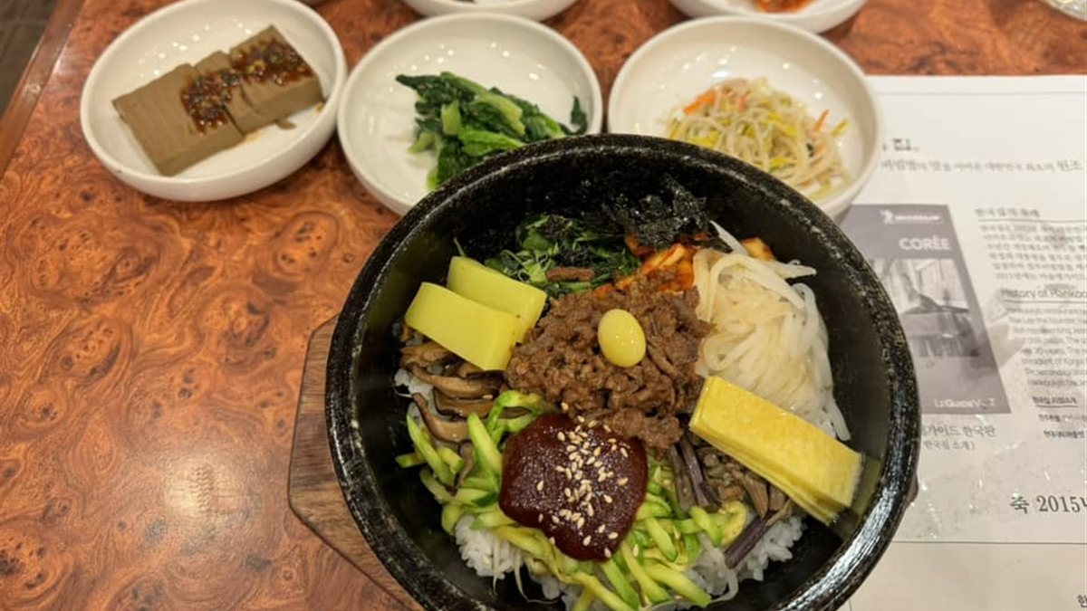 Jeonju bibimbap in a stone bowl topped with beef, vegetables and red pepper paste, with side dishes